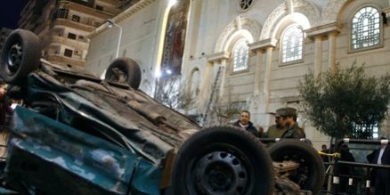 Policemen stand beside the wreckage of a car after a bomb blast outside the Coptic Orthodox church in Egypt's northern city of Alexandria