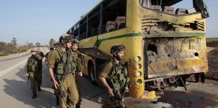 Israeli soldiers walk near a bus that was damaged by an anti-tank missile fired from the Gaza Strip into southern Israel
