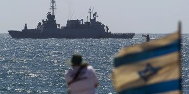 A man looks on as an Israeli navy boat maneuvers just outside the port of Ashdod