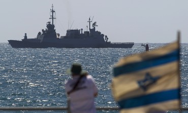 A man looks on as an Israeli navy boat maneuvers just outside the port of Ashdod